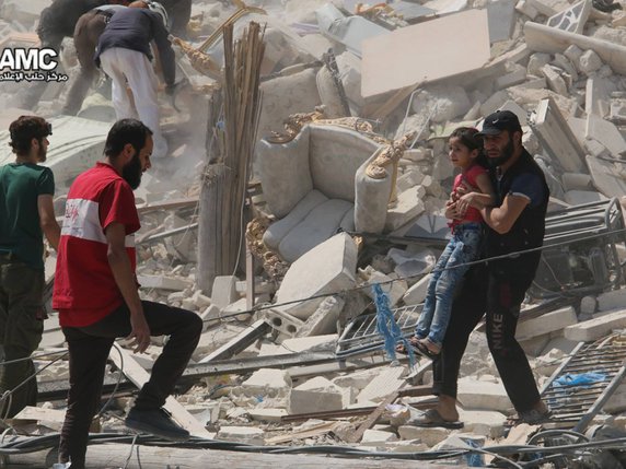 Un homme porte une fillette dans les débris après une attaque avec des barils d'explosifs cette semaine à Aleppo. © KEYSTONE/AP Aleppo Media Center/UNCREDITED