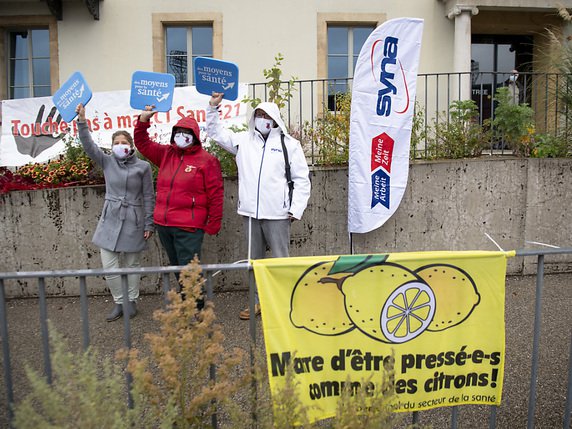 Des représentants des syndicats manifestent avec un masque de protection lors du lancement de cette semaine de protestation. Sur place devant l'Hôpital Pourtalès à Neuchâtel, seules 25 personnes, les travailleurs de la santé n'ayant apparemment pas été autorisés à sortir manifester. © KEYSTONE/LAURENT GILLIERON