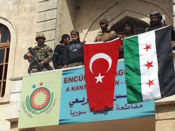 Perchés sur le balcon d'un bâtiment public d'Afrine, des soldats ont brandi le drapeau turc. Plus loin, des rebelles syriens se sont rassemblés au pied d'une statue d'une figure historique de la résistance kurde, déboulonnée. © Keystone/EPA/DHA / DOGAN NEWS AGENCY