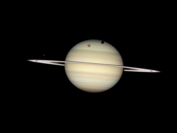 79 lunes connues tournent en orbite autour de Saturne, ici Titan et son ombre et à gauche Mimas. Les plus petites ne font que un kilomètre de diamètre (archives). © KEYSTONE/AP NASA