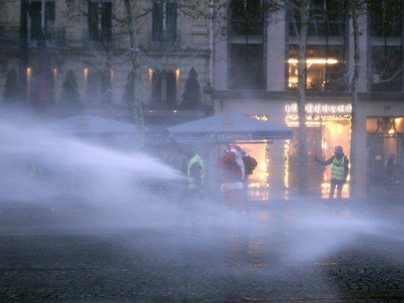 Sur les Champs-Elysées, la police a fait usage de canons à eau pour disperser quelques dizaines de manifestants, comme ce militant déguisé en Père Noël, à la nuit tombante © KEYSTONE/AP/KAMIL ZIHNIOGLU