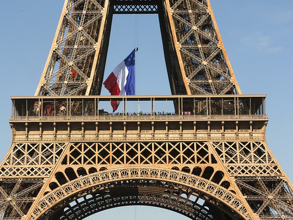 Un large drapeau français a été déployé le long d'un câble d'acier au niveau du 1er étage de la tour Eiffel. © KEYSTONE/AP/MICHEL SPINGLER